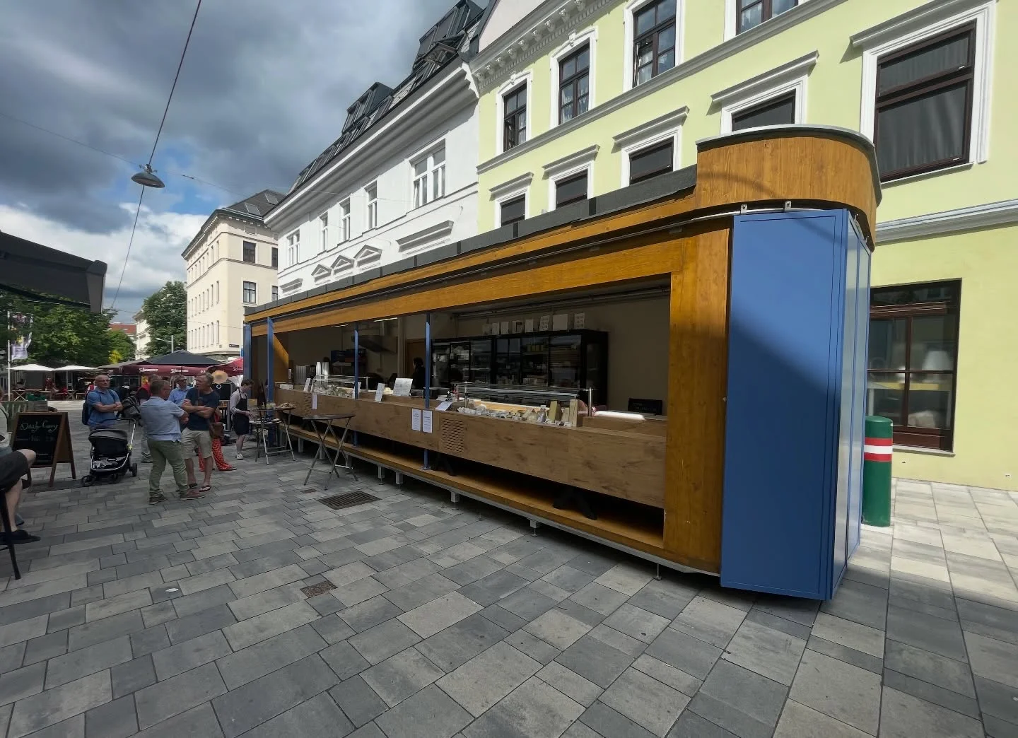 Der geöffnete kaes.at-Käsestand am Kutschkermarkt mit Holzfassade und blauen Türen